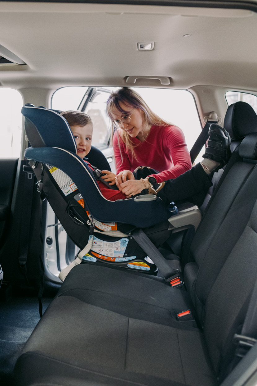 Parent securing a young child into a car seat facing the back of the car.