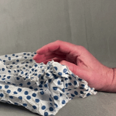 Close up of one hand crumpling a sheet of tissue paper into the palm of the hand.
