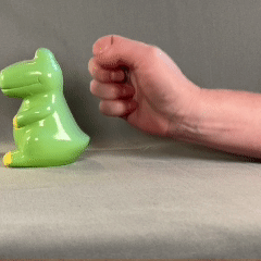 Close up of hand moving coins tucked in palm to fingertips and putting coin into a dinosaur piggy bank.