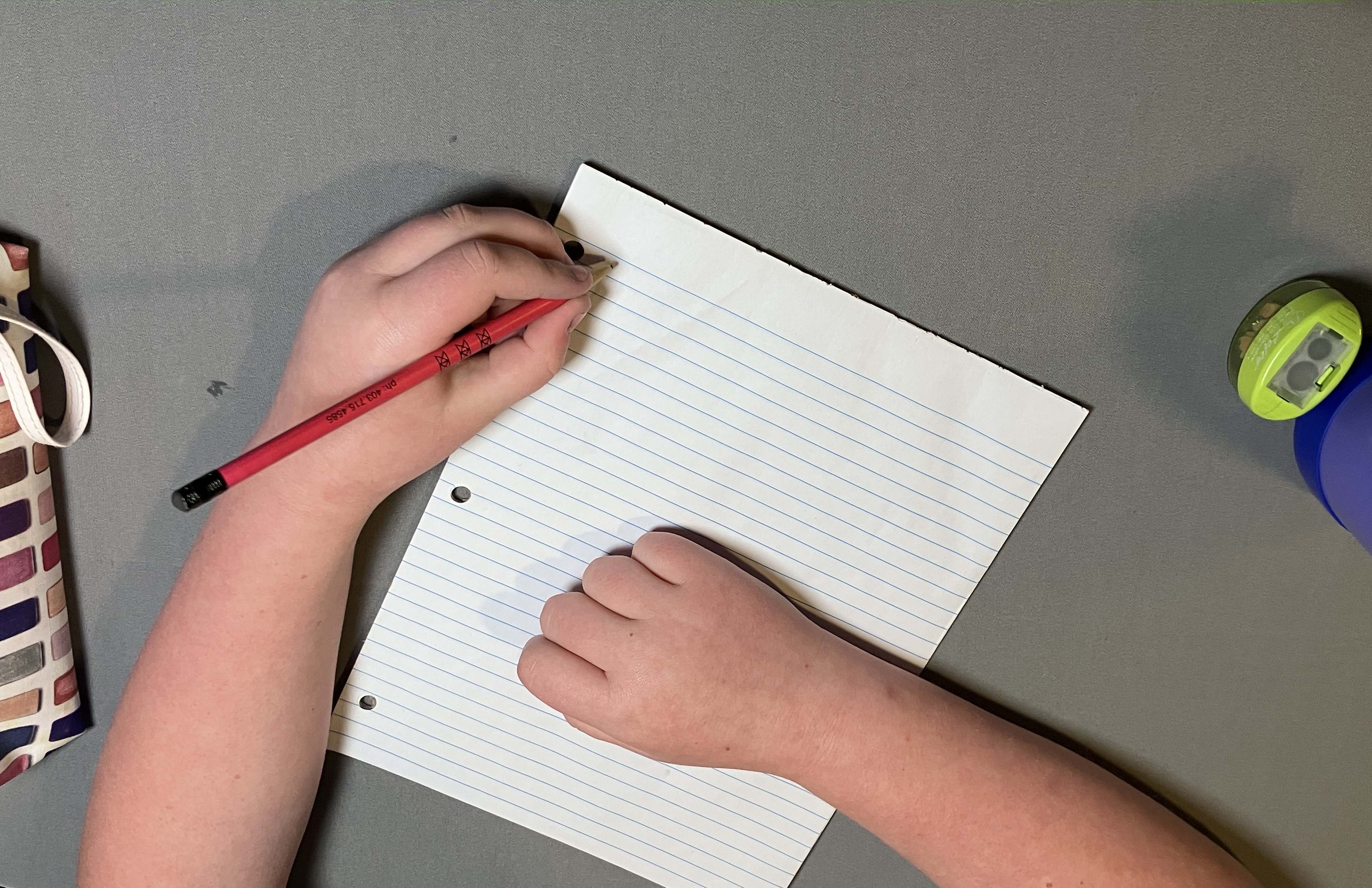 Child printing with page set up for left-handed writer. Paper tilted to the right, in line with their forearm. 