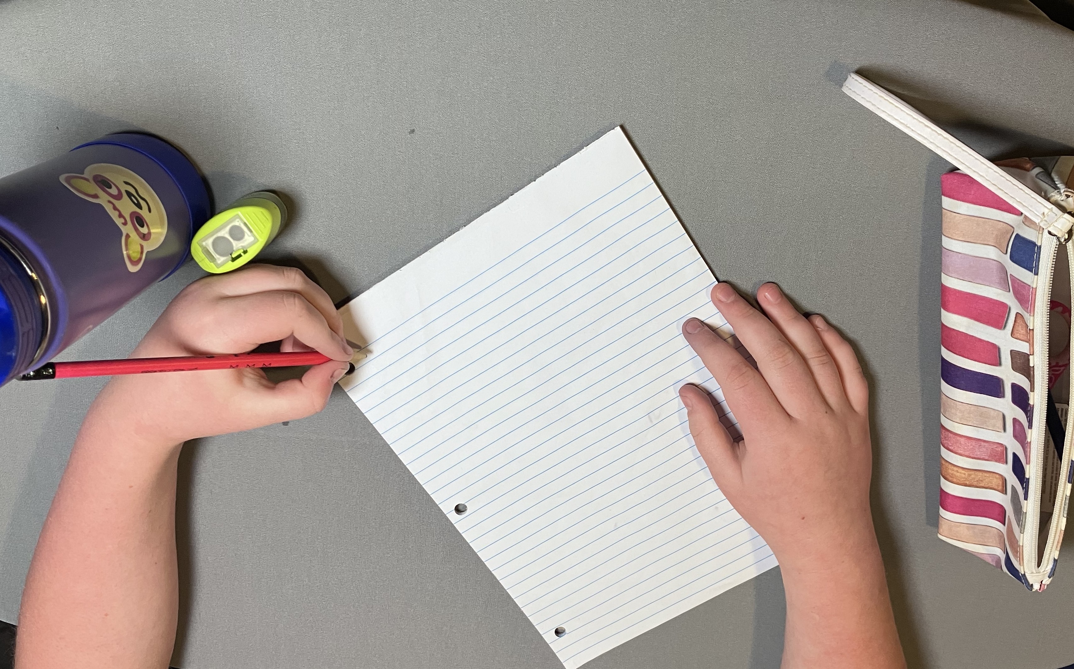 Left-handed child printing with right-handed page setup. Paper tilted to the left, wrist awkwardly bent, covering writing. 